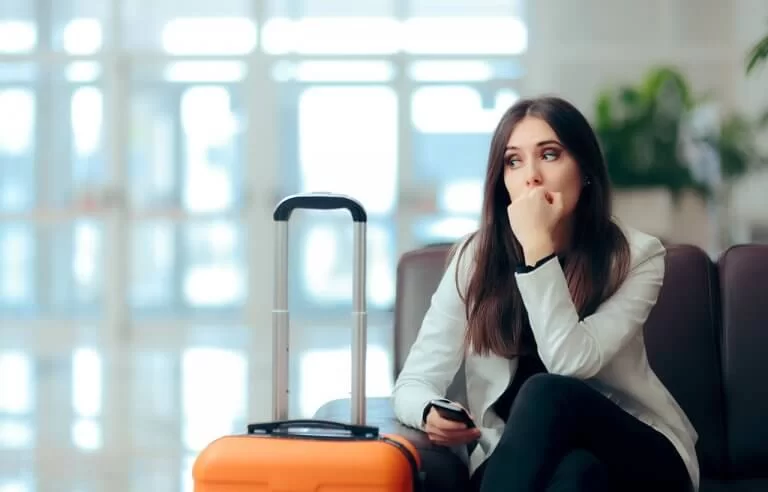Mulher com cara de preocupação sentada ao lado da mala de viagem no saguão do aeroporto