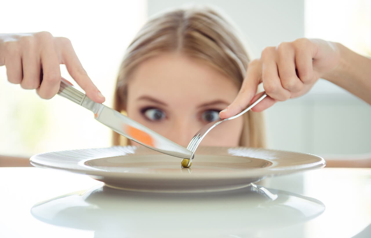 Mulher loira cortando um grão no prato de comida representando dieta restritiva