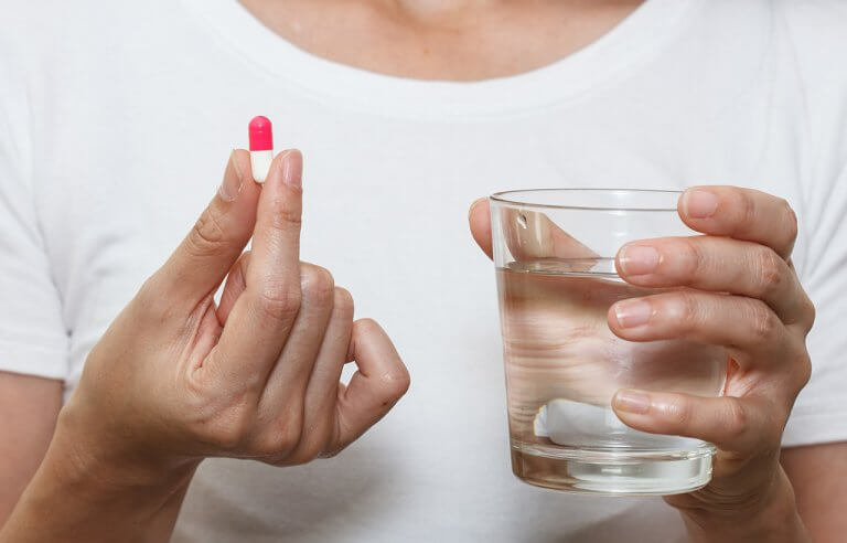 Mulher com um comprimido em uma das mãos e um copo de água na outra: tomando remédio