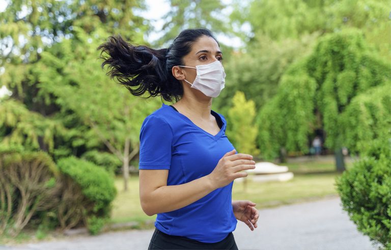 Mulher de máscara praticando corrida em meio a natureza: exercício físico ar livre