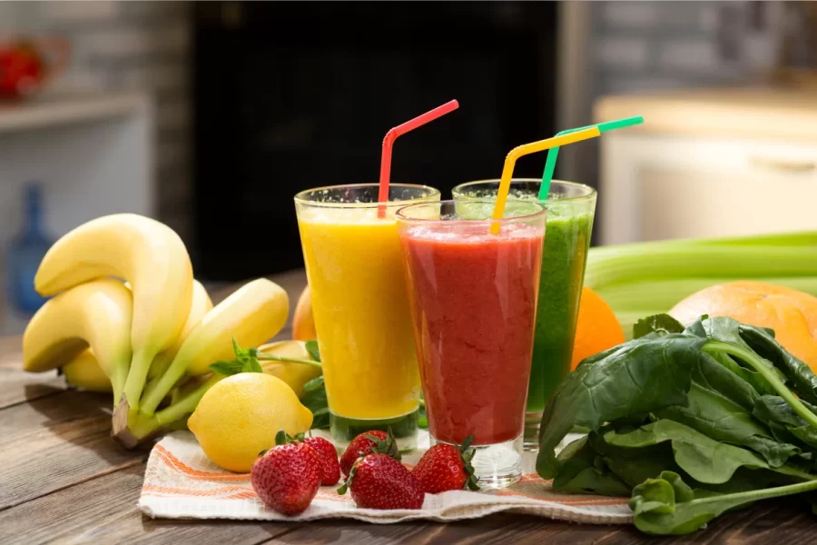 Alimentos saudáveis: 3 sucos de frutas naturais, banana,morango e verduras em cima da mesa